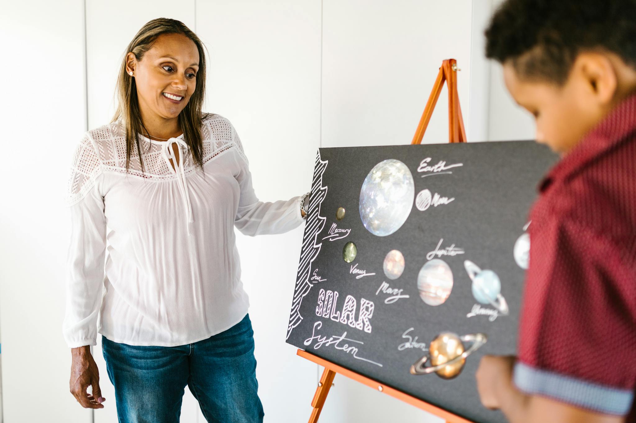A mother and son collaborate on a creative solar system school project indoors.