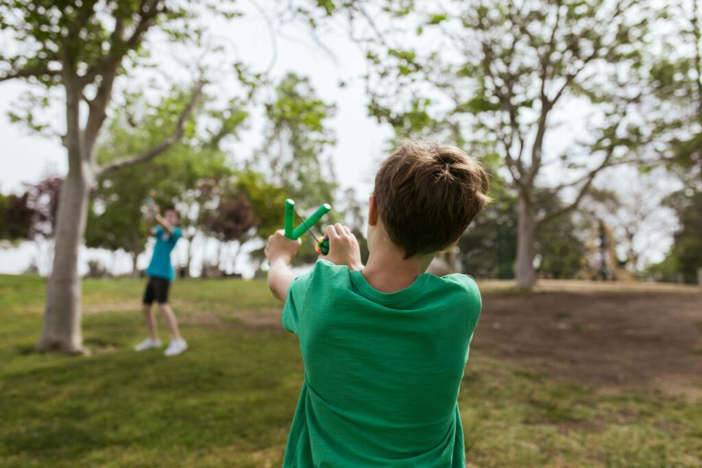 Children enjoy outdoor play with toy crossbows in a sunny park setting.